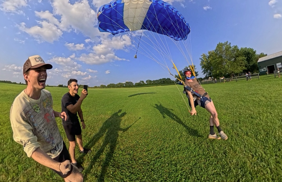 Friends cheering as a skydiver lands under canopy in a green field
